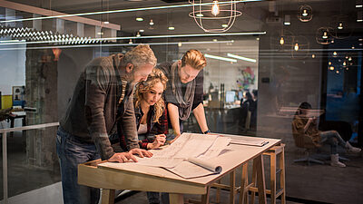 Three team members standing at a table reviewing blueprints