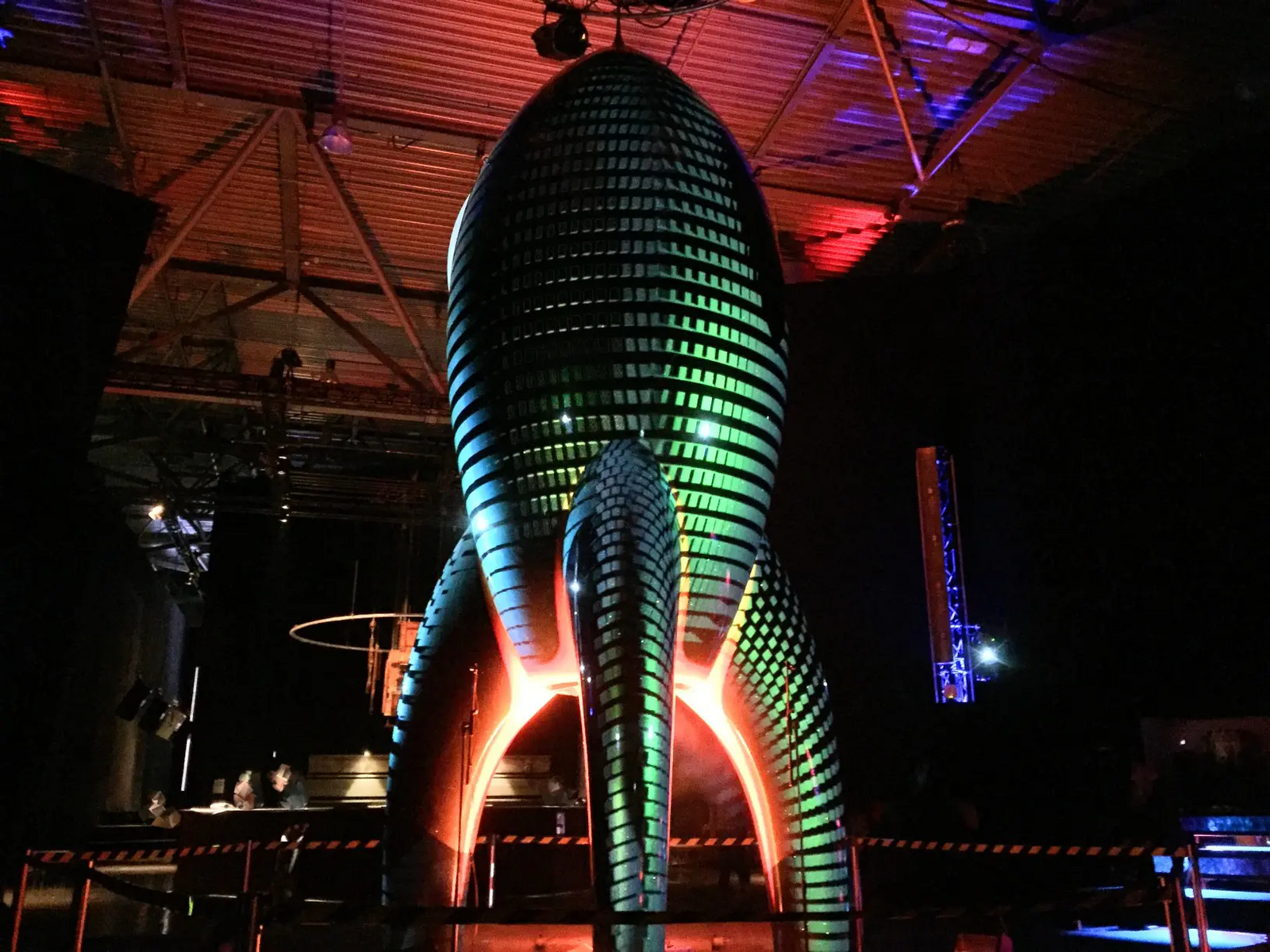 Innenraum eines dunklen Veranstaltungsortes mit einer großen, skulpturalen Lichtinstallation, die in bunten Farben leuchtet. Die Atmosphäre ist dunkel und atmosphärisch.