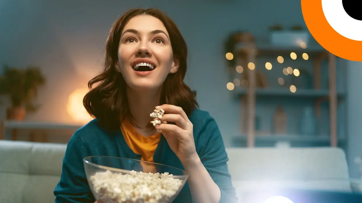 Une jeune femme mange du pop corn en regardant un film avec son vidéoprojecteur, avec un air enthousiaste.  