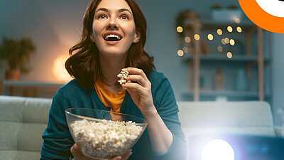 Une jeune femme mange du pop corn en regardant un film avec son vidéoprojecteur, avec un air enthousiaste.  