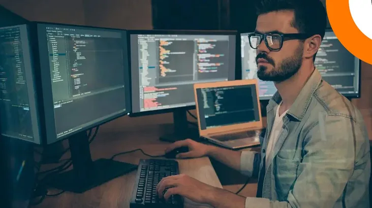 Un homme portant des lunettes travaille sur plusieurs ordinateurs. 
