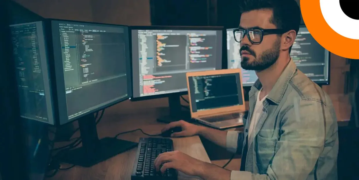 Un homme portant des lunettes travaille sur plusieurs ordinateurs. 