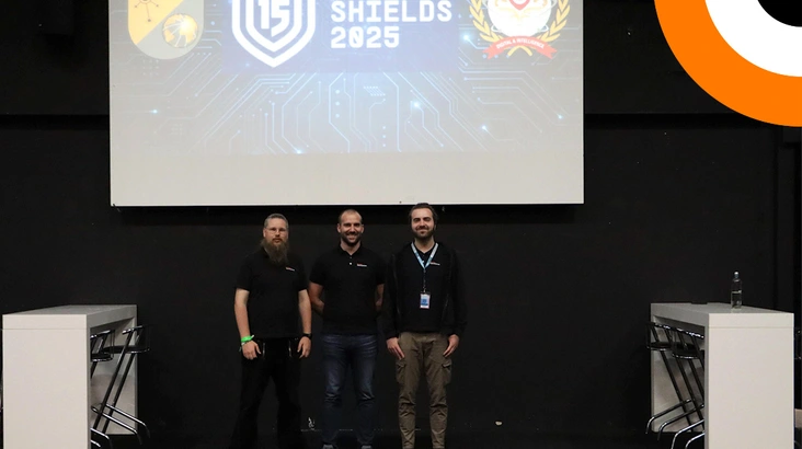 Orange Cyberdefense présent à Locked Shields 2025 Trois professionnels de la société Orange Cyberdefense se tenant côte à côte pendant un événement organisé par l'OTAN.
