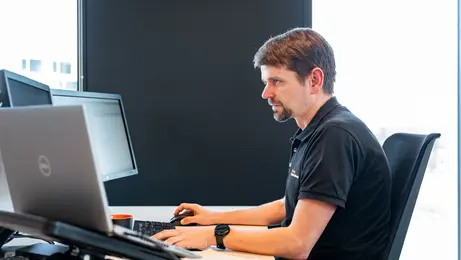 Un homme assis à son bureau travaille avec un ordinateur fixe au double écran en face de lui et un ordinateur portable.