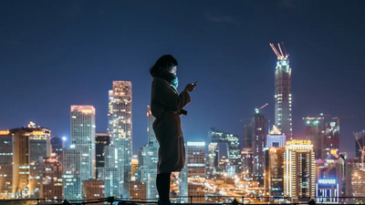 Eine Frau steht auf einem Dach vor einer nächtlichen Skyline mit Wolkenkratzern.