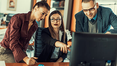 Three people huddled around a computer monitor