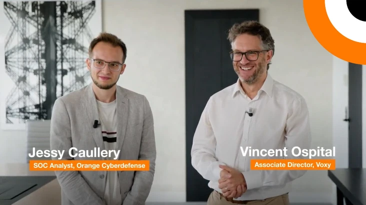 Deux professionnels en cybersécurité se tiennent côte à côte en souriant pour les besoins d'un témoignage vidéo.  