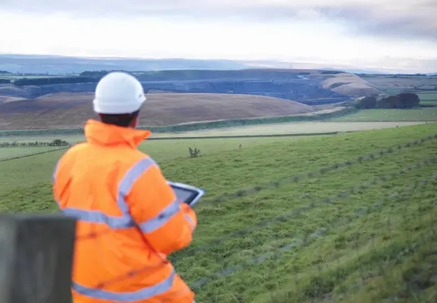 Land surveyor in an orange work suit standing in a field