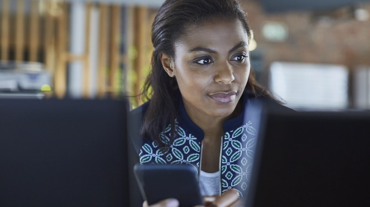 Une femme consulte un message sur son mobile et regarde son écran d'ordinateur