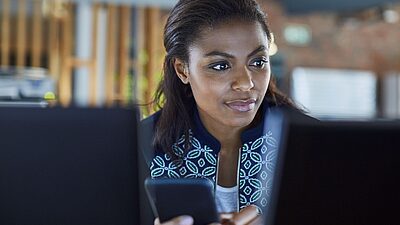 Une femme consulte un message sur son mobile et regarde son écran d'ordinateur