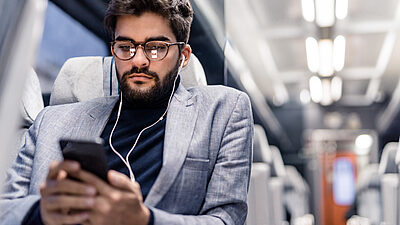 A man with headphones, on a train listening to something on his mobile device