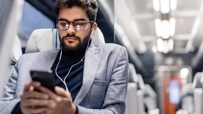 A man with headphones, on a train listening to something on his mobile device