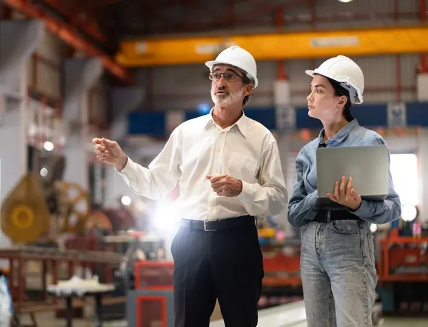 Senior engineer and colleague with a laptop inspecting operations in an industrial plant