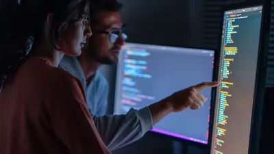 Two people analyzing code on a monitor