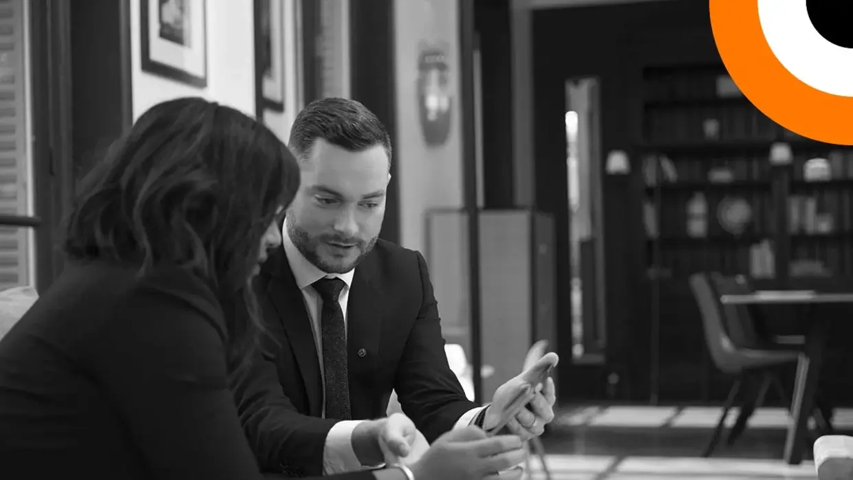 Un homme et une femme bien habillés sont assis côte à côte et regardent une tablette. 