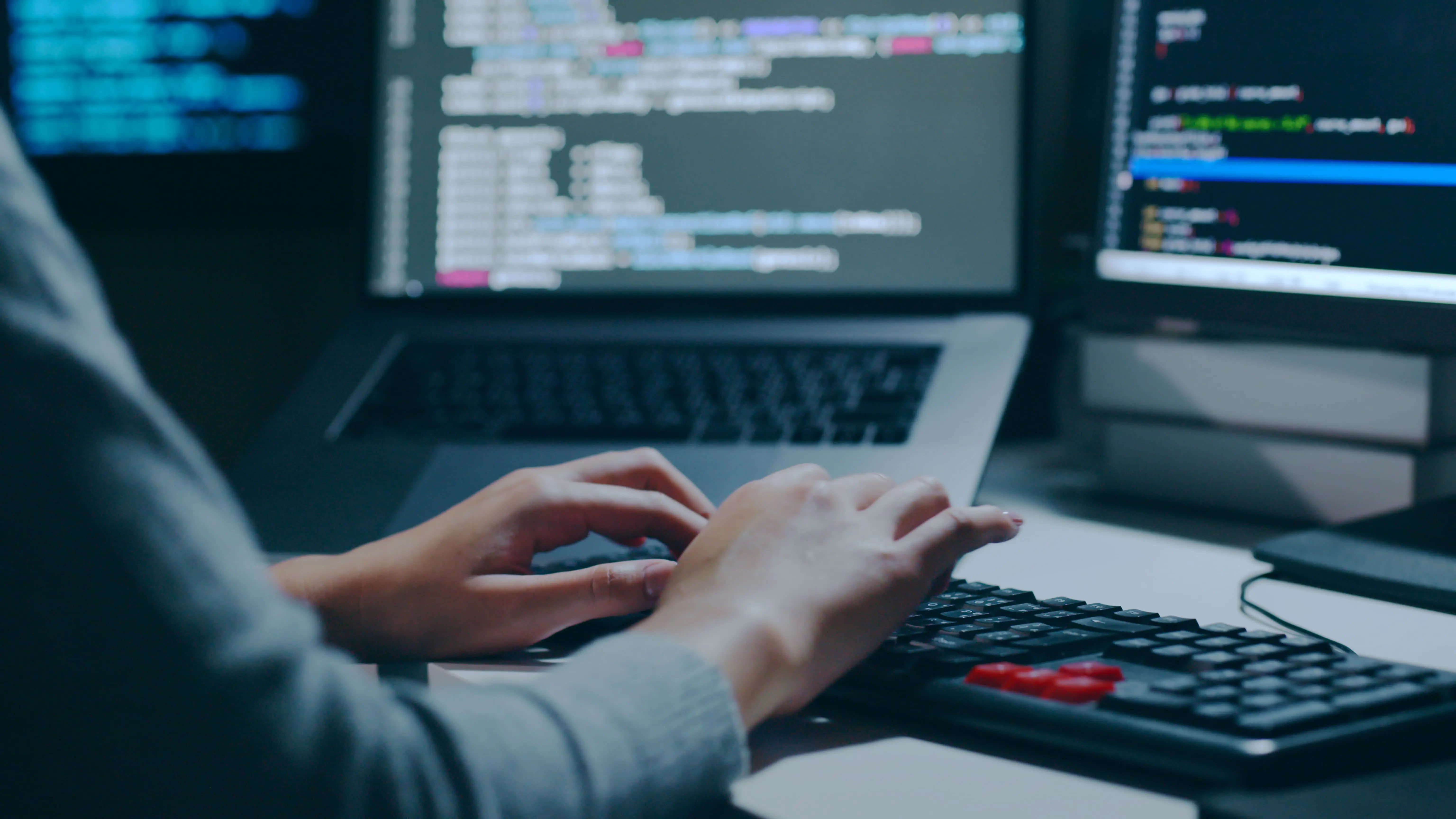 A person working on a computer with multiple screens displaying code, highlighting a cybersecurity or programming environment.