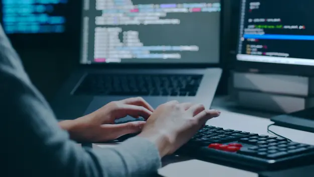 A  person working on a computer with multiple screens displaying code, highlighting a cybersecurity or programming environment.